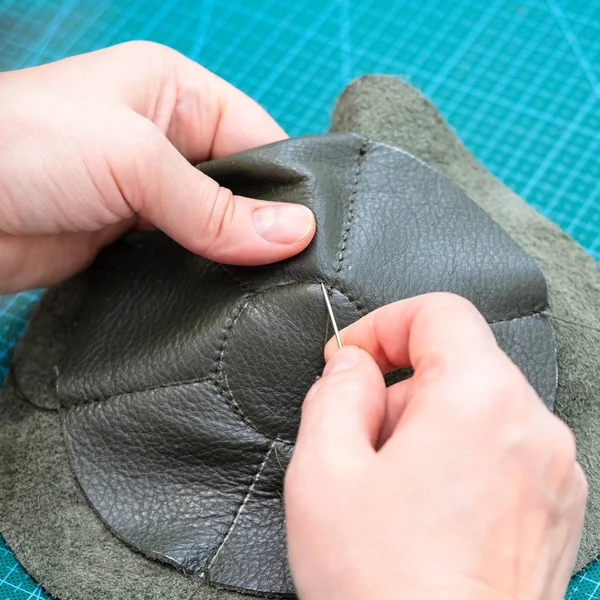 workshop of making the leather bag for jewelry - craftsman sews inner bottom of the pouch by needle