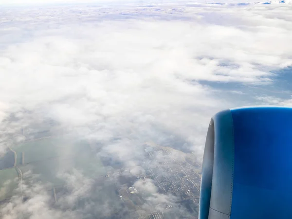 view of airplane turbine and country fields under clouds during flight through porthole