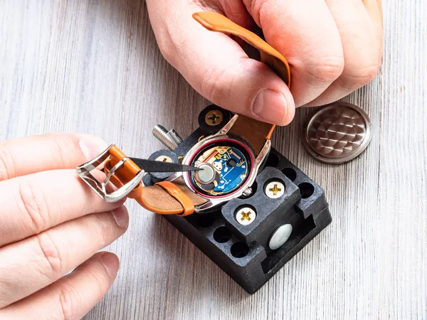 watch repairer workshop - watchmaker changes battery in quartz wristwatch with plastic tweezers on wooden table