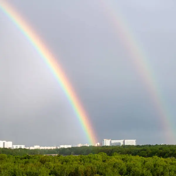 double rainbow over green forest and city on spring day