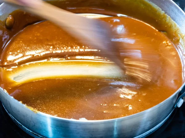 cooking salted butter caramel sauce at home kitchen - stirring hot smooth prepared salty caramel dessert with wooden culinary spatula in steel pan