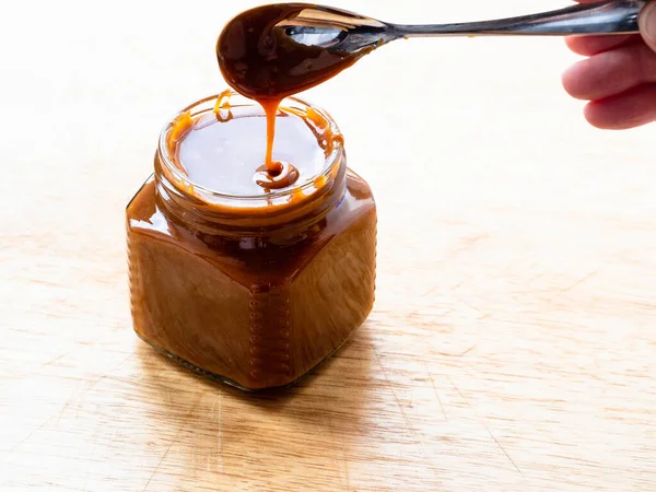 cooking salted butter caramel sauce at home kitchen - homemade smooth cooked salty caramel dessert in open glass jar on wooden board