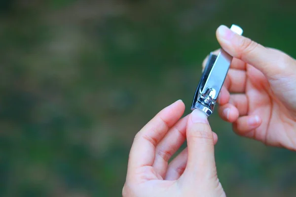 woman cut finger nail on nature green background