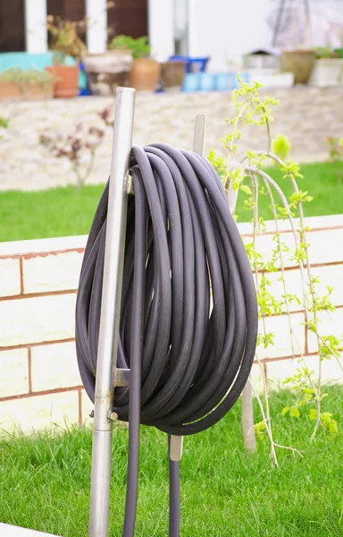 Black garden hose for watering is wound on a special stand. Stand for a hose in the garden, on the green grass. Garden at home on a summer sunny day. Selective focus image.
