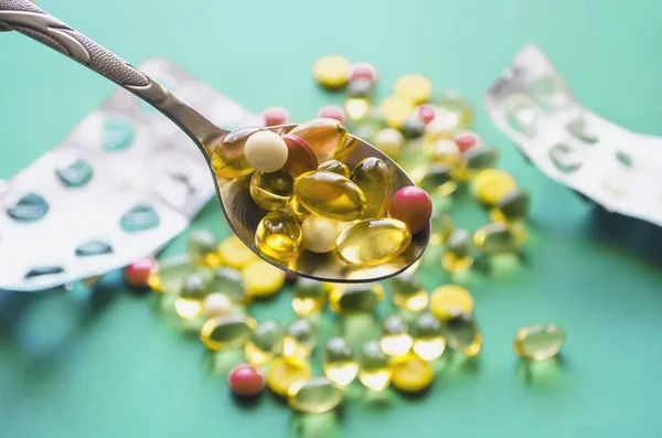 Gümüş metal kaşık, parlak pembe ve sarı tabletler, Omega-3 yağ kapsülleri. Mavi bir arka plan üzerinde haplar, kapsüller ve boş ilaç paketleri vardır. Görüntünün seçici odağı, yakın çekim.