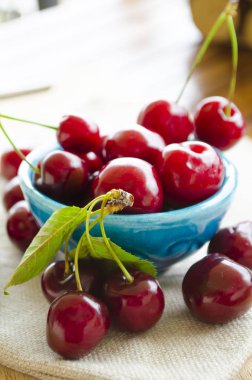 Parlak sulu kırmızı meyveler ve mavi emaye seramik kase tatlı kiraz yaprakları. Yakın çekim, seçici odak görüntüsü.