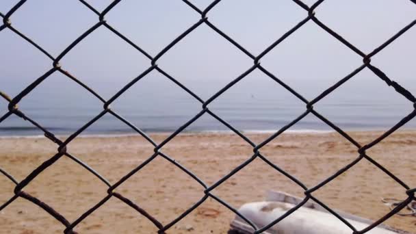 Rejilla de malla de metal. Playa arenosa mar azul claro. Vista de la playa a través de valla — Vídeos de Stock