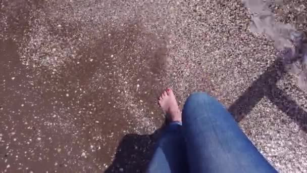 Joven camina a lo largo de la orilla del mar. Piernas femeninas en jeans azules. Primer plano . — Vídeos de Stock