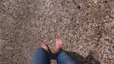 Genç bir kadın deniz kıyısında yürüyor. Kot pantolonlu kadın bacakları. Yakın plan..