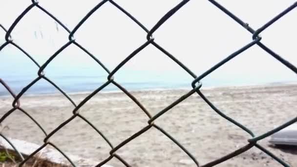 Metal netting grill. Sandy seashore clear blue sea. View of beach through fence — Stock Video