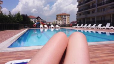 Beyaz kadın bacakları. Yakın plan. Kadın karşı havuzda güneşleniyor..