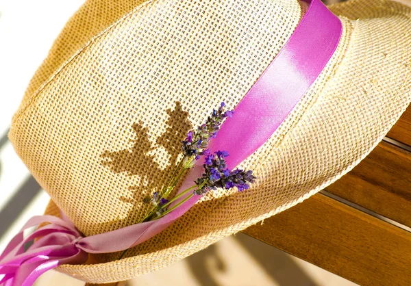 Light straw hat on wooden brown table. Lilac-pink ribbon on hat of woman\'s hat. bouquet of dry lavender in rustic wicker straw basket.