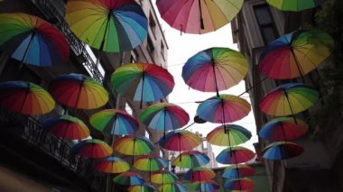 Birçok renkli gökkuşağı açık şemsiyeler evler arasında dar bir caddede asılı.