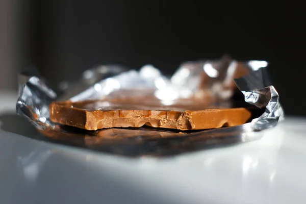 Sütlü çikolata kahve rengi hafif bir arka plan üzerinde gümüş folyo barlarda bir parça