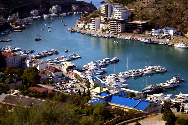 Sea port city by the sea. Yachts on the pier in the blue sea. White boats and yachts in the port city against the backdrop of green mountains. Balaclava in the Crimea.