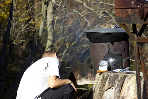 Camping and cooking a man in a cauldron and herbal tea on a fire. A man prepares food in nature on a clear day in a cauldron. Food during a picnic in a kettle and a cauldron on a fire.