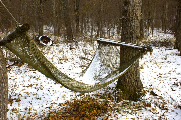 Winter holidays in the forest. Hammock in the snow in the woods of an abandoned forester's house. An isolated hammock in the forest among the trees.