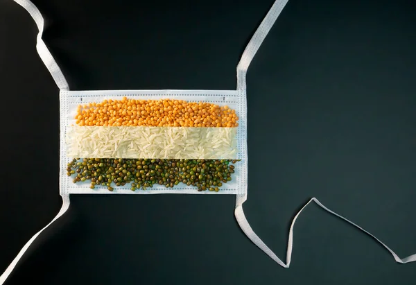 Turuncu beyaz ve yeşil gıda taneleri siyah arka planda izole edilmiş Hint bağımsızlığını temsil etmek için cerrahi bir maske takıyorlar.