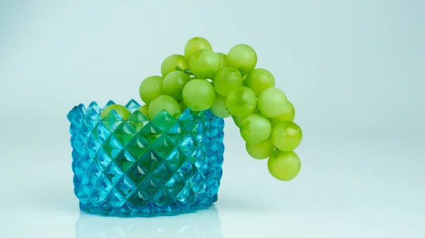 Beyaz zeminli mavi cam kasede yeşil üzümler 
