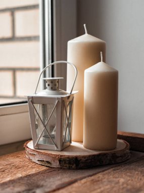 Dekoratif fener şamdanı ve beyaz mumlar pencere pervazındaki ahşap tepside.