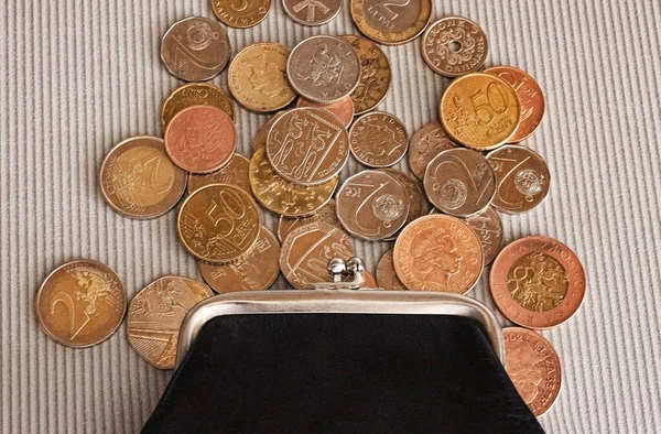 Many different coins from different countries from the black wallet are scattered around the table: dollars, pounds, rubles, pennies, cents, yuan. Saving money, losing finance, earning.