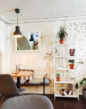 Vyborg, Rusya - 3 Mayıs 2020, minimalist iç mimari, beyaz tuğla duvarlar, bir kafe masası ve kitap ve ev bitkileriyle dolu bir kitaplık