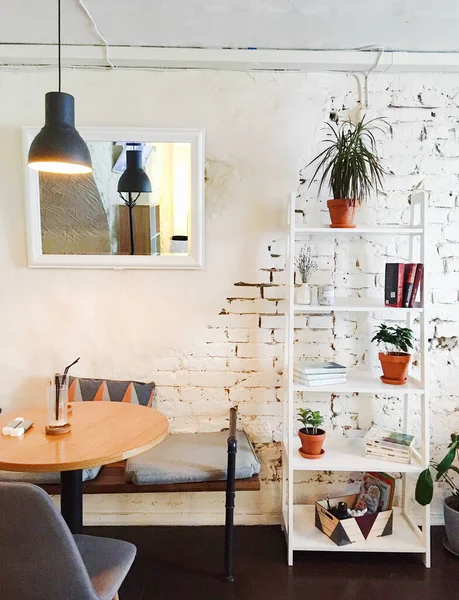 Vyborg, Rusya - 3 Mayıs 2020, minimalist iç mimari, beyaz tuğla duvarlar, bir kafe masası ve kitap ve ev bitkileriyle dolu bir kitaplık