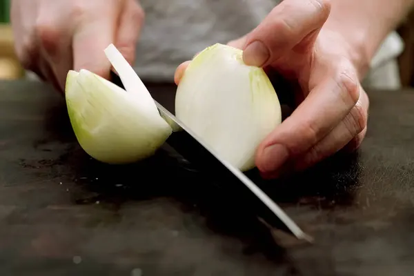Snijden van uien op een snijplank in de keuken. — Stockfoto