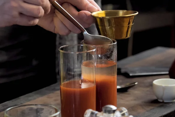 Pouring tomato juice into glasses through spoon. — Stock Photo, Image