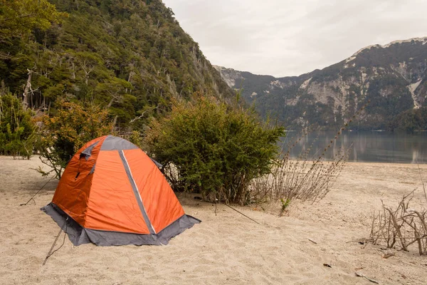 Camping orange tent in a campsite near a lagoon / Camping gear / Camping on the beach next to a lake with cloudy sky