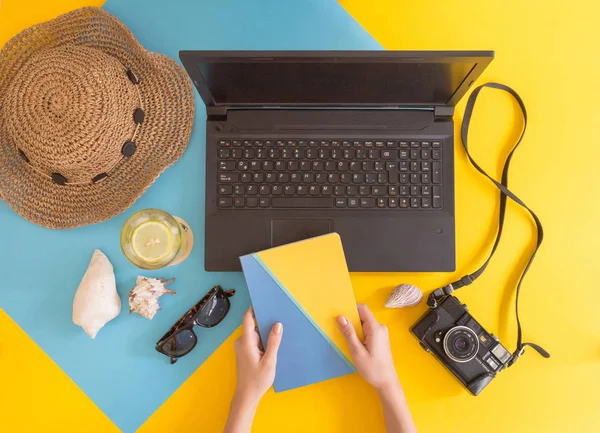 Flat lay work and travel, beach and tropical theme, with woman hands and copy space for text. Top view of workplace and vacation concept with blank space with summer or spring accesories on yellow and blue background