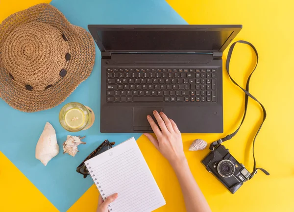 Flat lay work and travel, beach and tropical theme, with woman hands and copy space for text. Top view of workplace and vacation concept with blank space with summer or spring accesories on yellow and blue background