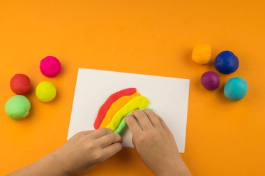 Çocuk bir gökkuşağı renkli hamuru oluşturur. Turuncu arka plan. Malzemeler ve araçlar için modelleme. Çocuk eller.