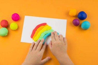 Çocuk bir gökkuşağı renkli hamuru oluşturur. Turuncu arka plan. Malzemeler ve araçlar için modelleme. Çocuk eller.