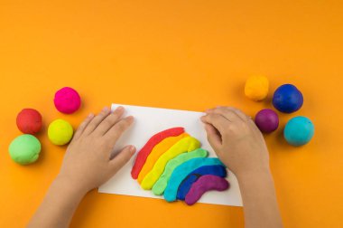 Çocuk bir gökkuşağı renkli hamuru oluşturur. Turuncu arka plan. Malzemeler ve araçlar için modelleme. Çocuk eller.