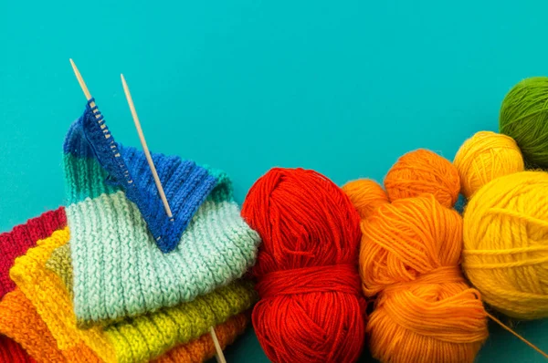 Knitting a rainbow scarf and hat. Basket with balls of wool, knitting needles. Blue background. Favorite work is a hobby.