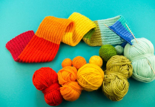 Knitting a rainbow scarf and hat. Basket with balls of wool, knitting needles. Blue background. Favorite work is a hobby.