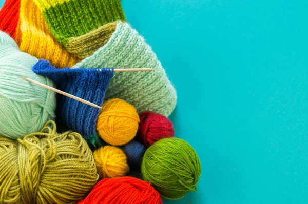 Knitting a rainbow scarf and hat. Basket with balls of wool, knitting needles. Blue background. Favorite work is a hobby.