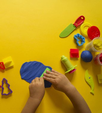 Çocuk kalıpları renkli hamuru üzerinden. Sarı arka plan. Malzemeler ve araçlar için modelleme. Çocuk eller.