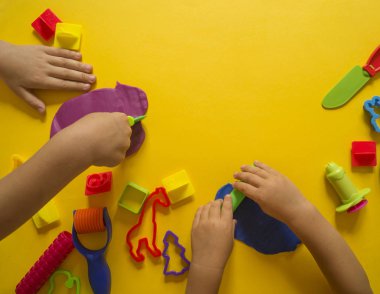 Çocuk kalıpları renkli hamuru üzerinden. Sarı arka plan. Malzemeler ve araçlar için modelleme. Çocuk eller.