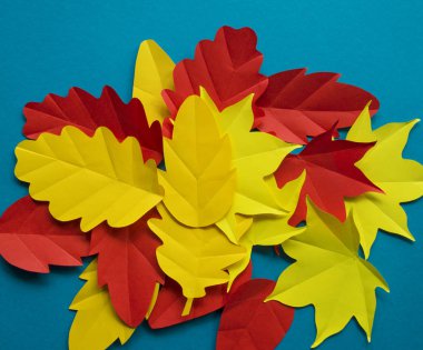 Kağıt yaprakları kırmızı, turuncu, sarı yaprak düşme düşmek. Mavi arka plan. El yapımı origami.