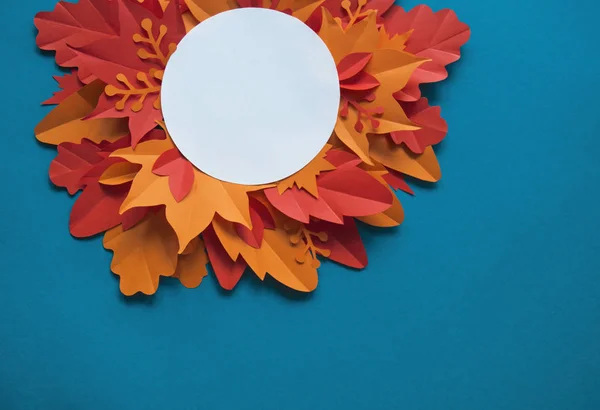 Leaves of paper autumn in a circle. Red, yellow and orange leaves. Place for recording. Blue background.