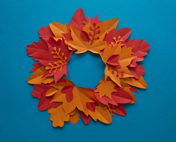 Leaves of paper autumn in a circle. Red, yellow and orange leaves. Place for recording. Blue background.