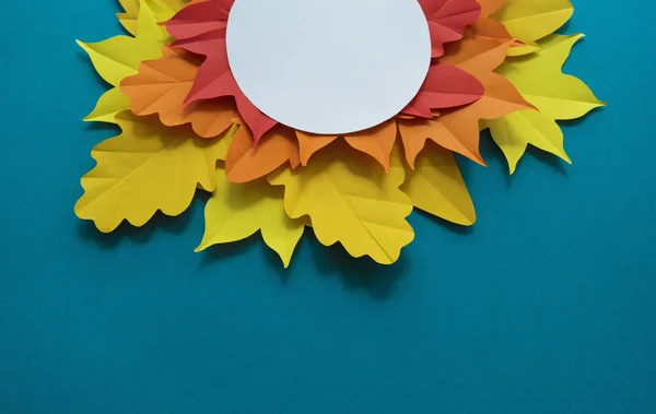 Leaves of paper autumn in a circle. Red, yellow and orange leaves. Place for recording. Blue background.