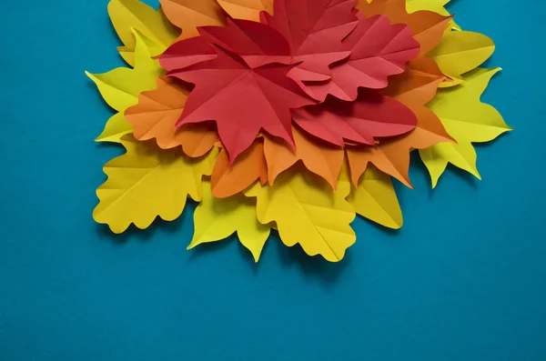 Leaves of paper autumn in a circle. Red, yellow and orange leaves. Place for recording. Blue background.