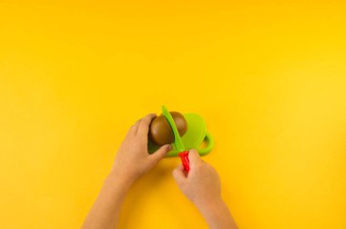 Bir çocuk bir gemide bir plastik meyve keser. Çocuk eller. Aşçı oynuyor. sarı arka plan.