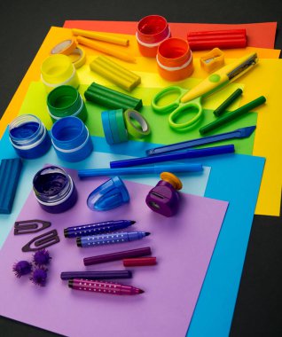 Okul aksesuarları gökkuşağı şeklinde ortaya konur. Siyah arka plan. Okul öğrencisine mutlu. Çocuklar için sanat ve el sanatları. Gökkuşağı renkleri, alfabe harfleri ve sayıları öğrenen çocuk.