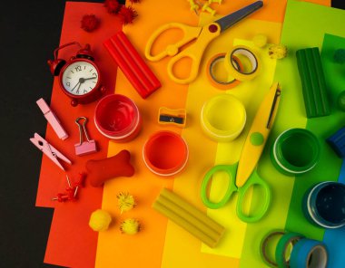 Okul aksesuarları gökkuşağı şeklinde ortaya konur. Siyah arka plan. Okul öğrencisine mutlu. Çocuklar için sanat ve el sanatları. Gökkuşağı renkleri, alfabe harfleri ve sayıları öğrenen çocuk.