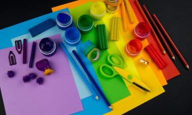 Okul aksesuarları gökkuşağı şeklinde ortaya konur. Siyah arka plan. Okul öğrencisine mutlu. Çocuklar için sanat ve el sanatları. Gökkuşağı renkleri, alfabe harfleri ve sayıları öğrenen çocuk.