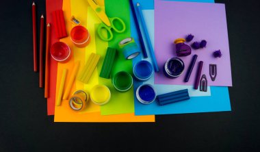 Okul aksesuarları gökkuşağı şeklinde ortaya konur. Siyah arka plan. Okul öğrencisine mutlu. Çocuklar için sanat ve el sanatları. Gökkuşağı renkleri, alfabe harfleri ve sayıları öğrenen çocuk.